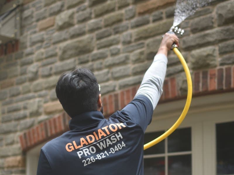 Over-the-shoulder view of a technician rinsing a stone wall