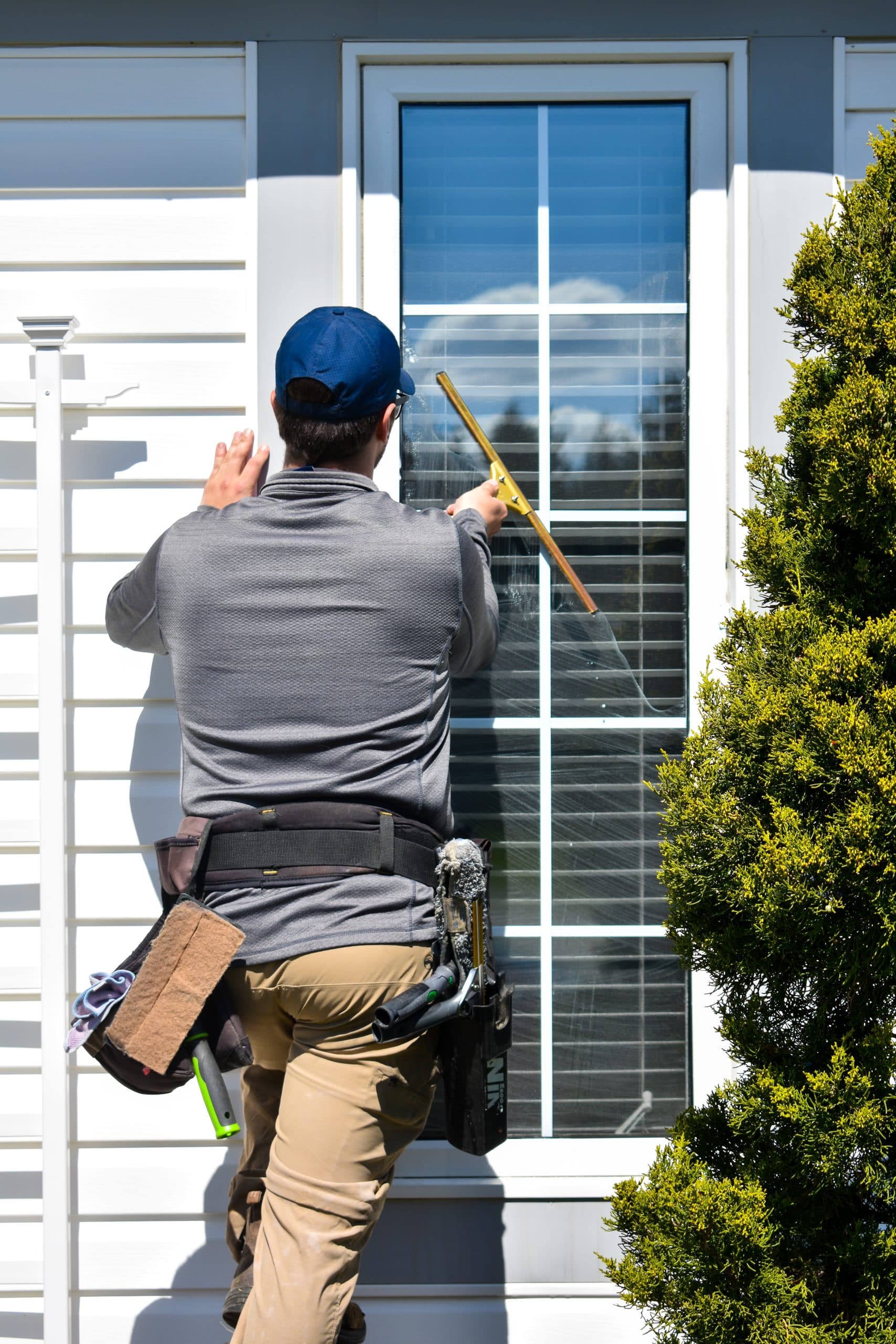 A technician on a ladder detailing a colonial-pane window on gray siding