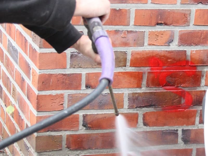 A red graffiti tag being removed from a brick wall